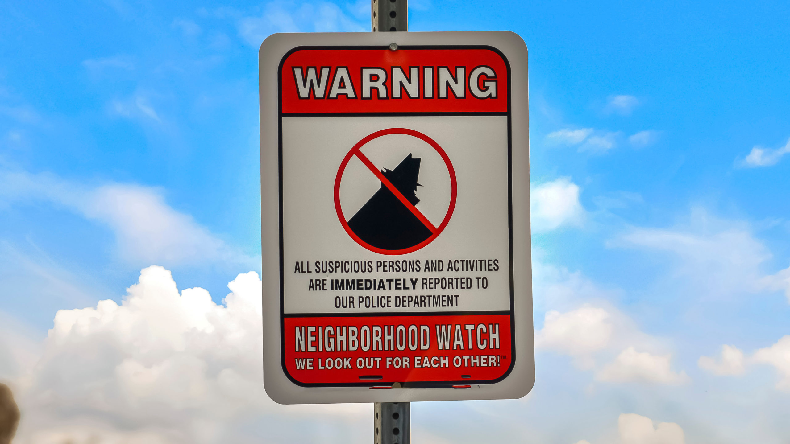 Red and white street sign that reads "neighborhood watch" against a blue sky.